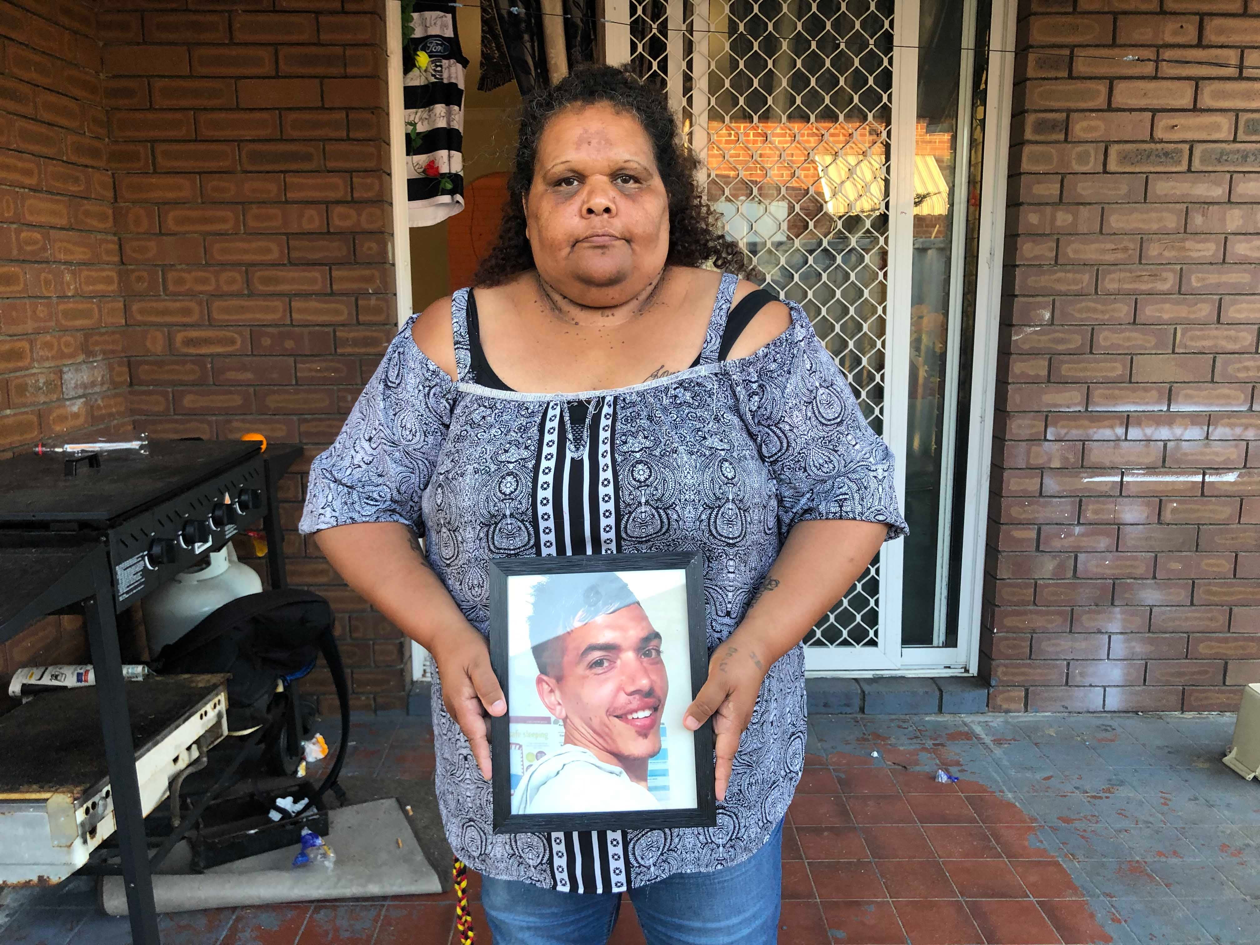 A woman holds a framed photo of a young man