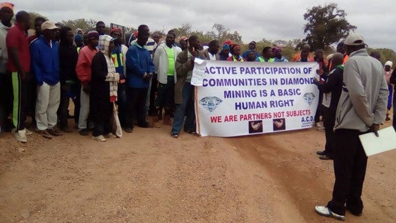 A group of protesters holds a sign that reads "Active Participation of Communities in Diamond Mining is a Basic Human Right."