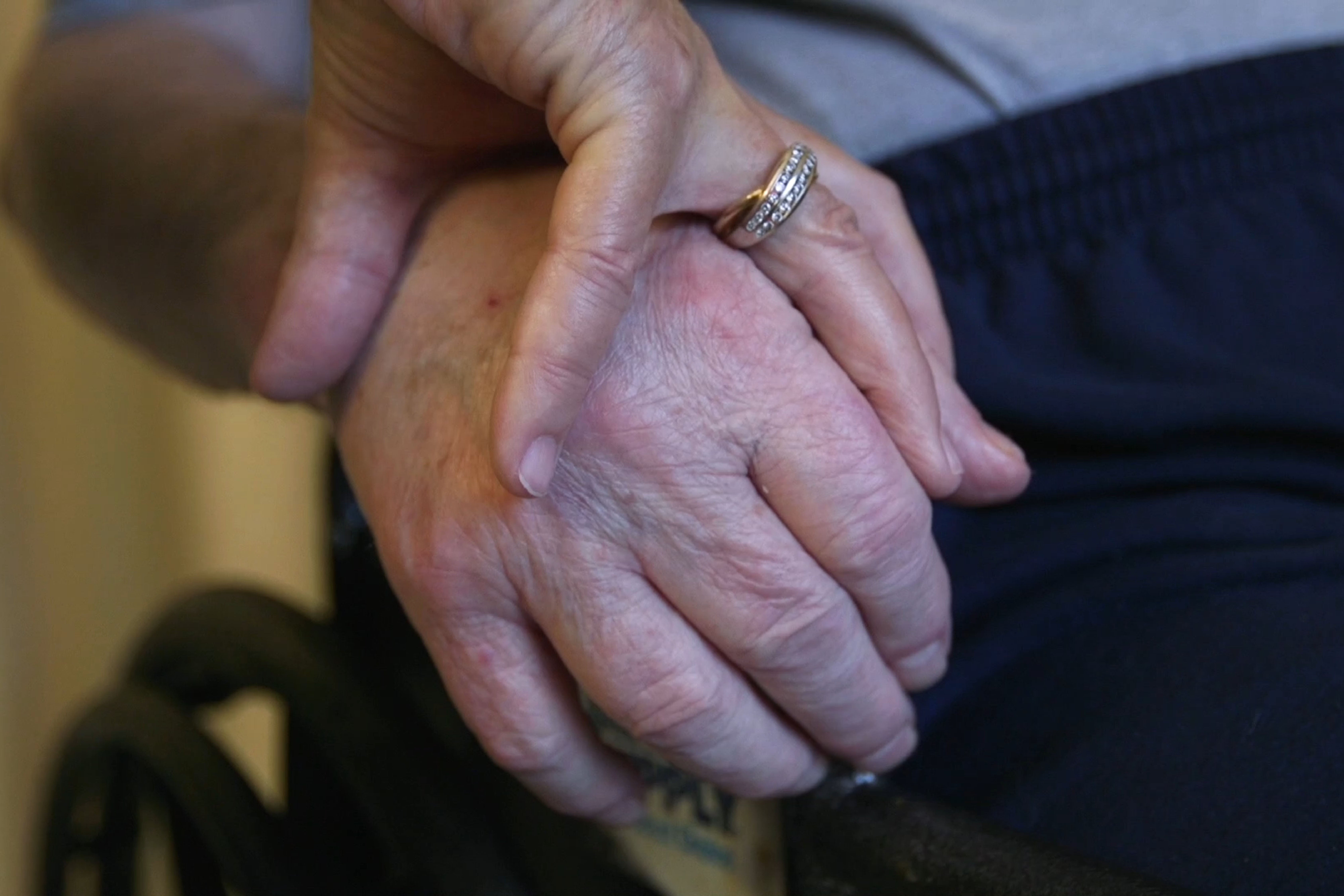 A nursing home resident holds his wife’s hand. 