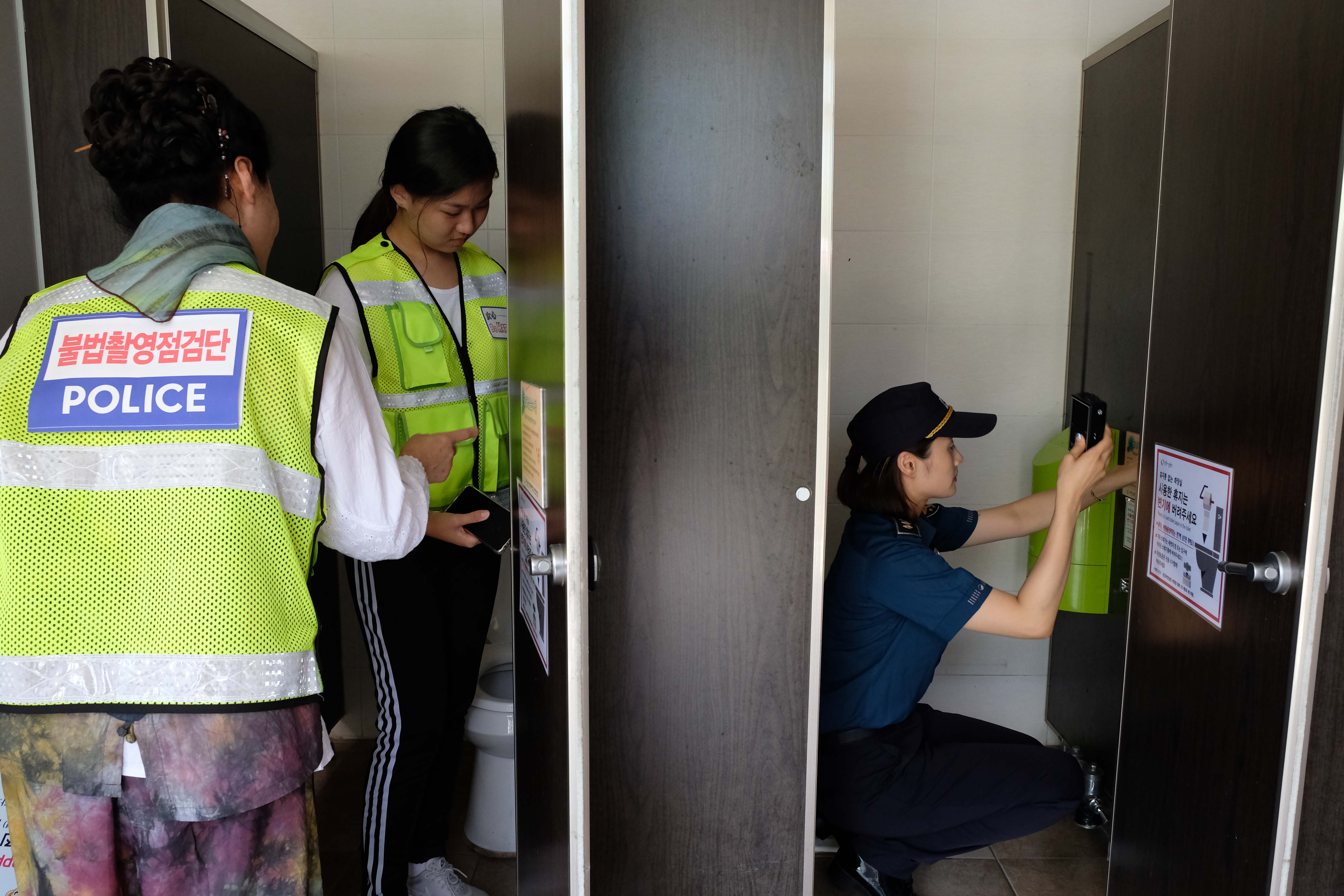 Three women investigate a bathroom stall