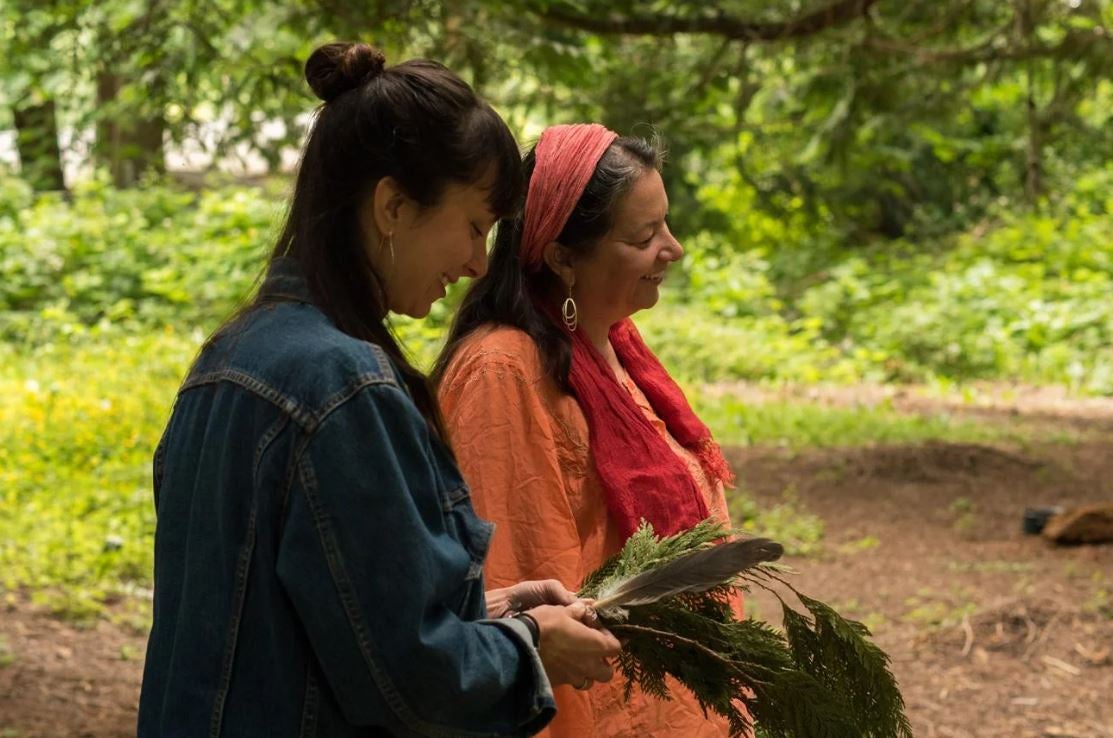 Two women stand together in the woods