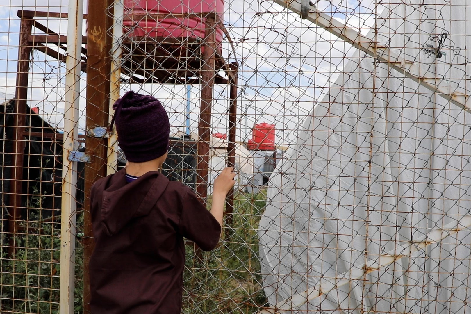 A boy stares through a fence