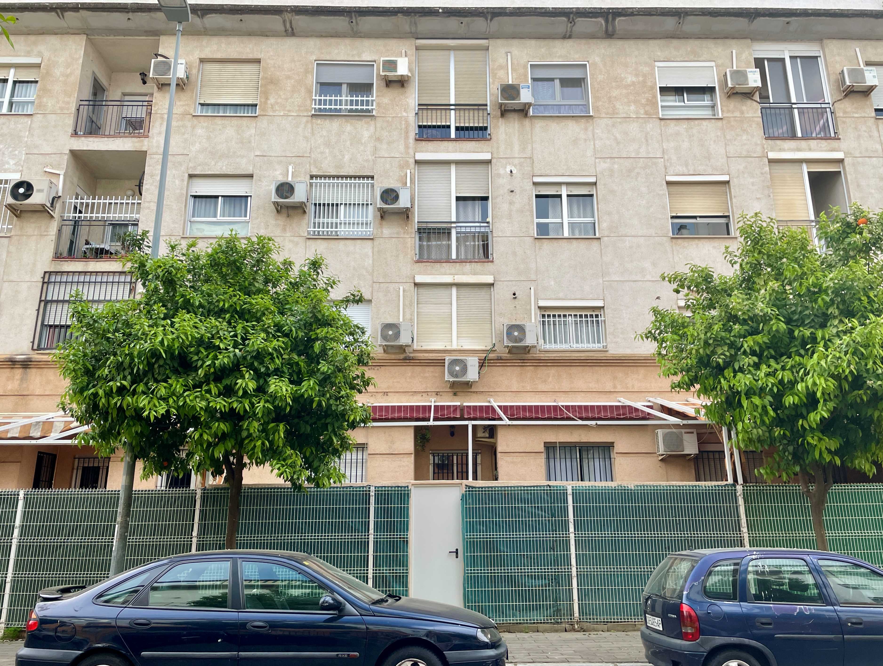 The front of a residential building in Seville (Andalusia, Spain), with outside air conditioning units and two green trees.