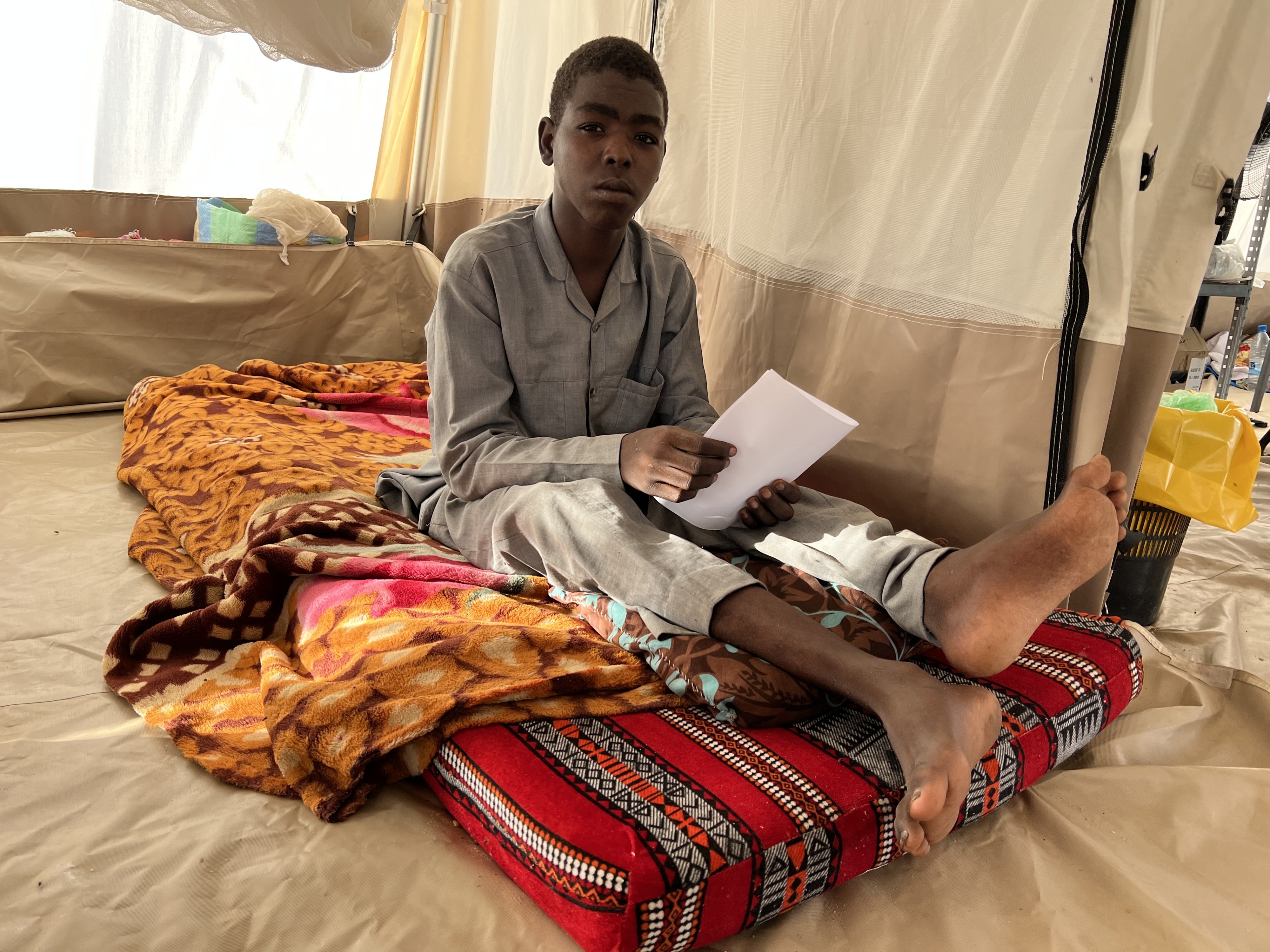 A teenage boy sits in a tent hospital