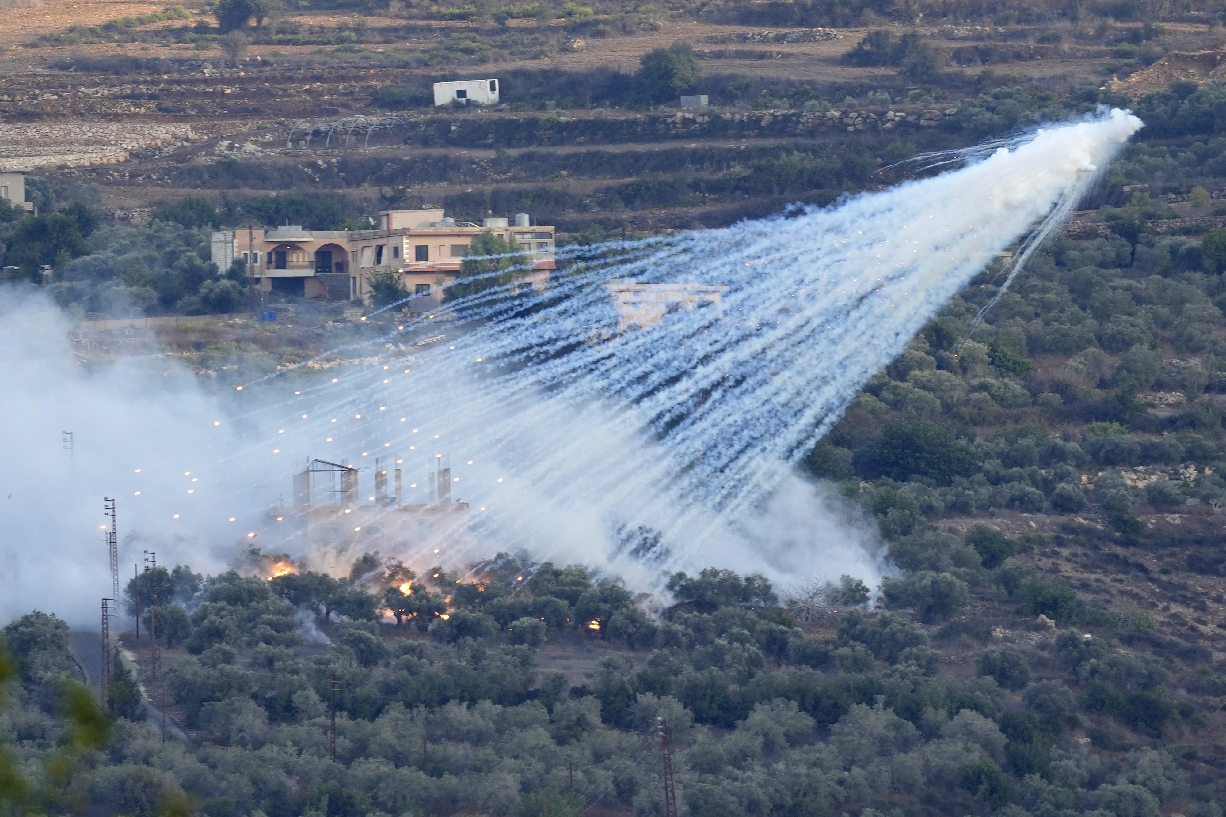 Artillery projectile containing white phosphorus bursts over a village