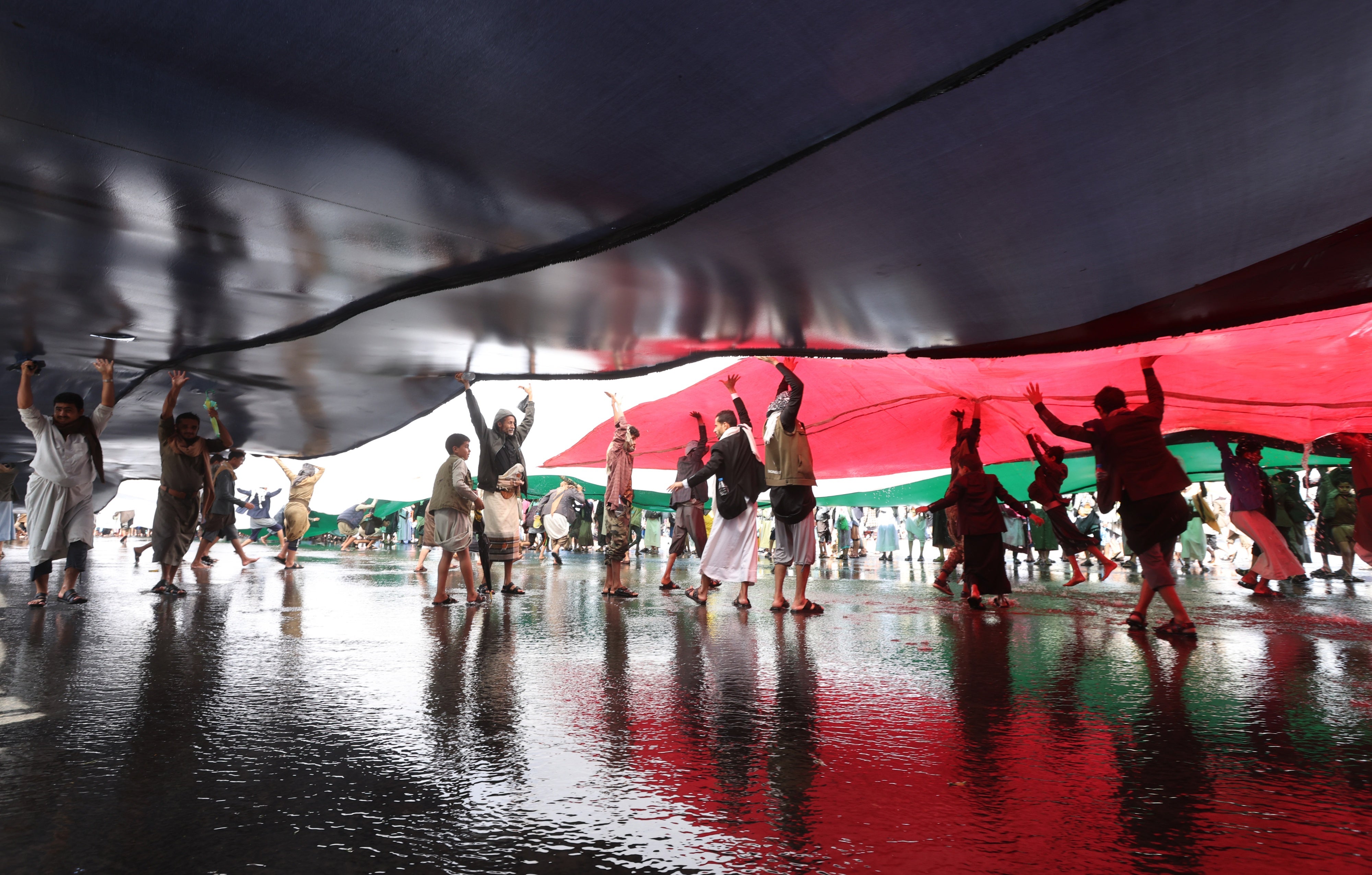 People stand beneath large flags at a protest