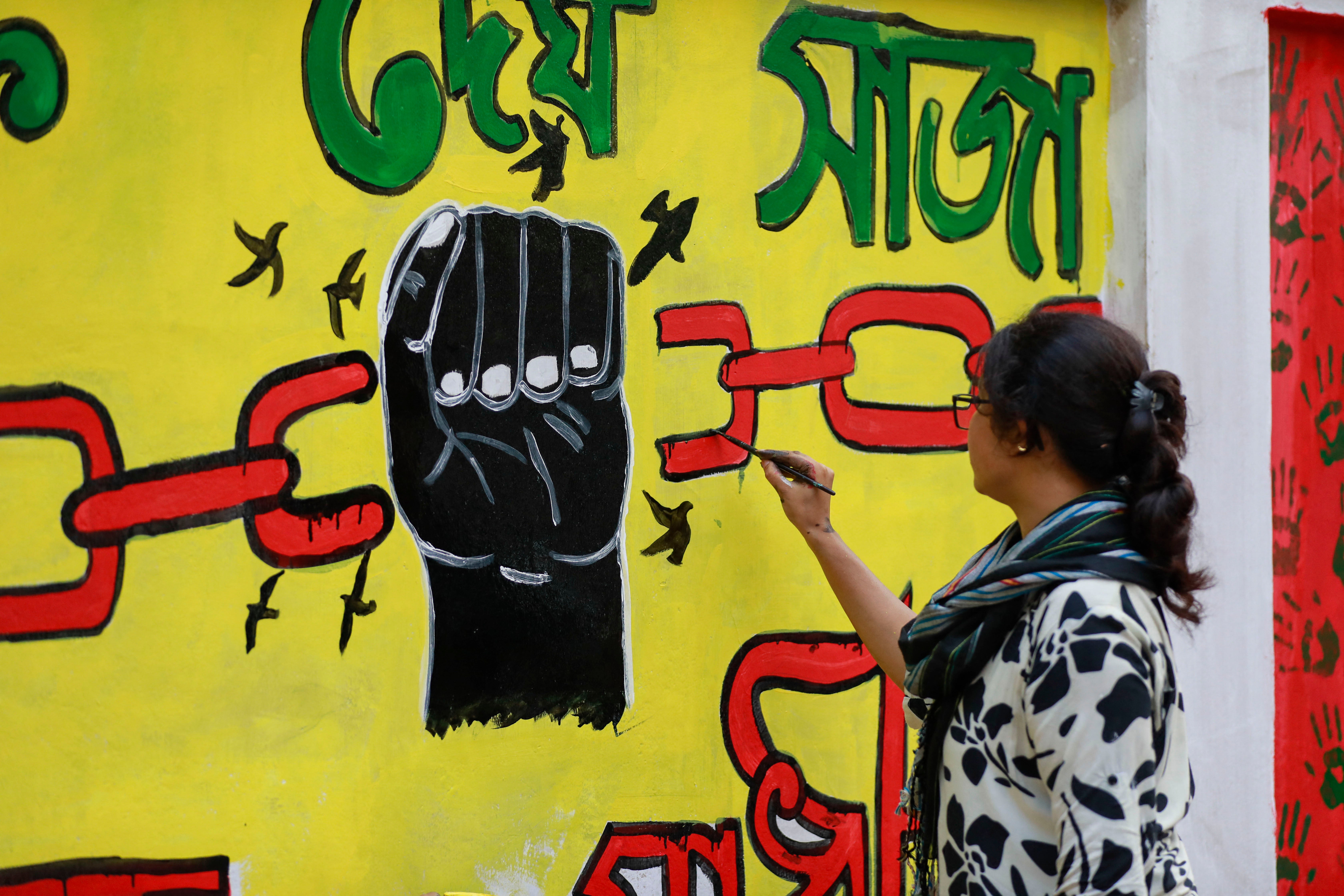 A student paints street art of a fist breaking chains