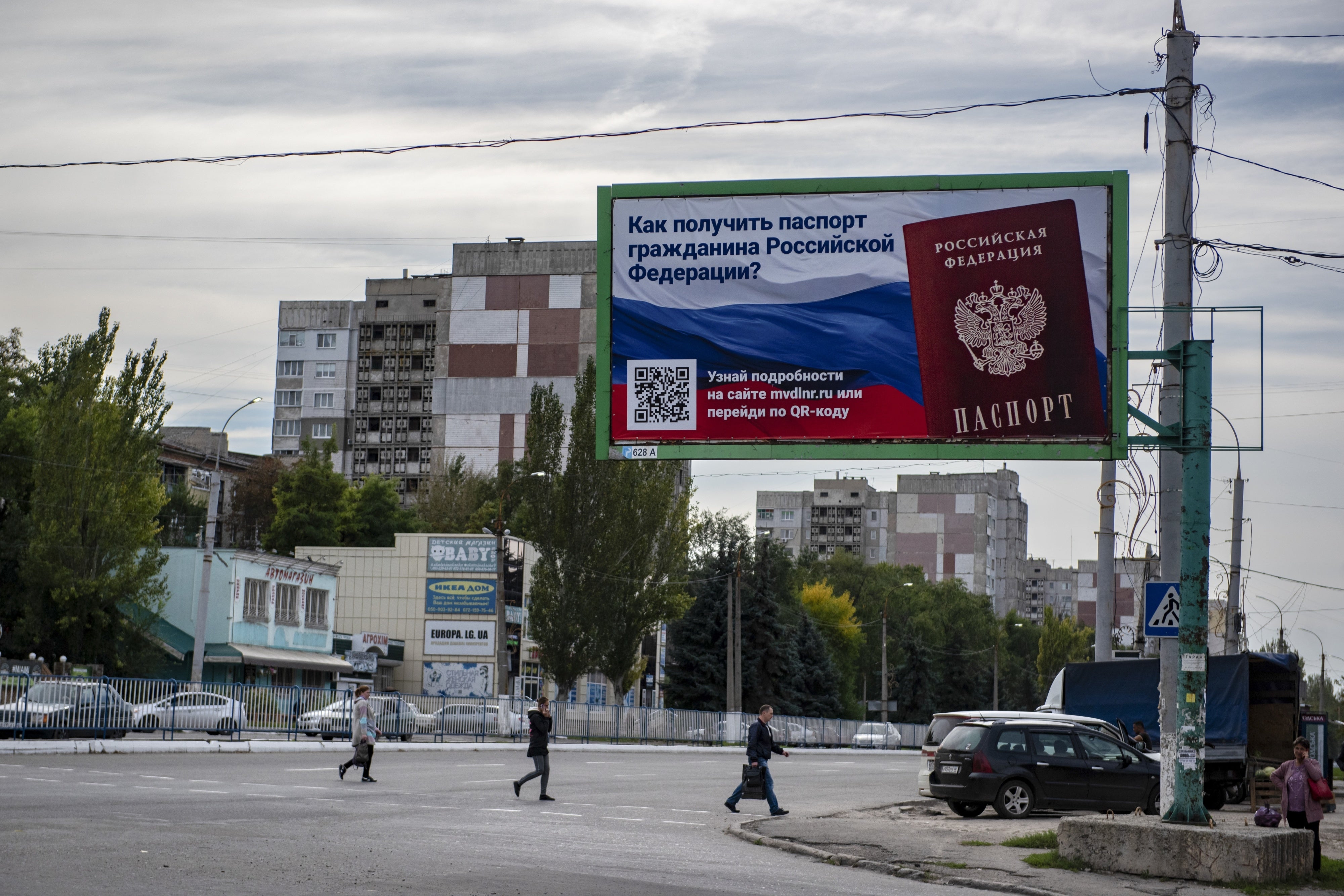 Menschen überqueren eine Straße mit einer Plakatwand, auf der zu lesen ist: „Wie man einen Pass als Bürger Russlands erhält“, im besetzten Gebiet von Luhansk, 22. September 2022.