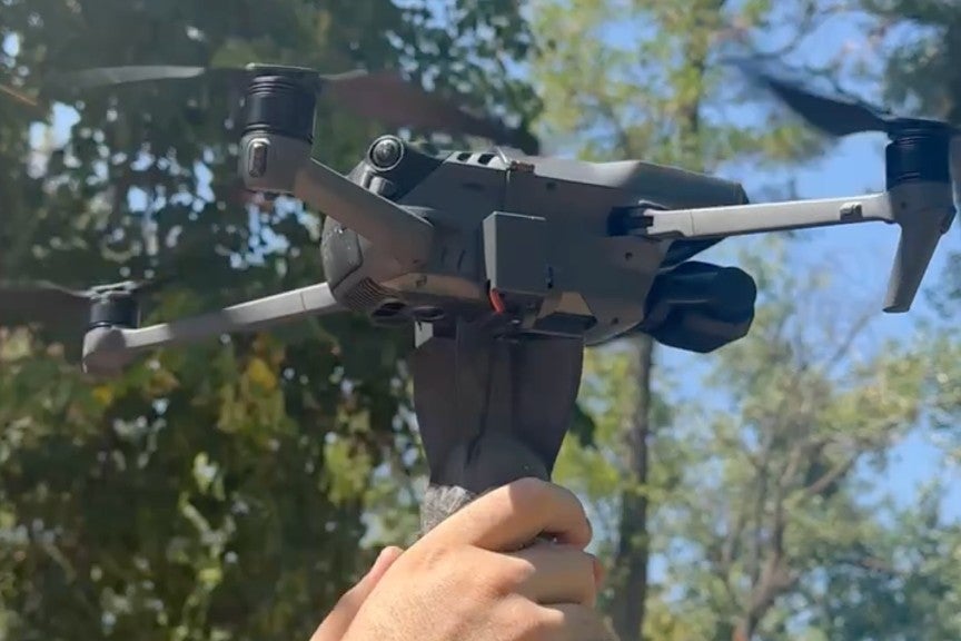 a DJI Mavic drone hovering while an individual attaches a munition to its airframe