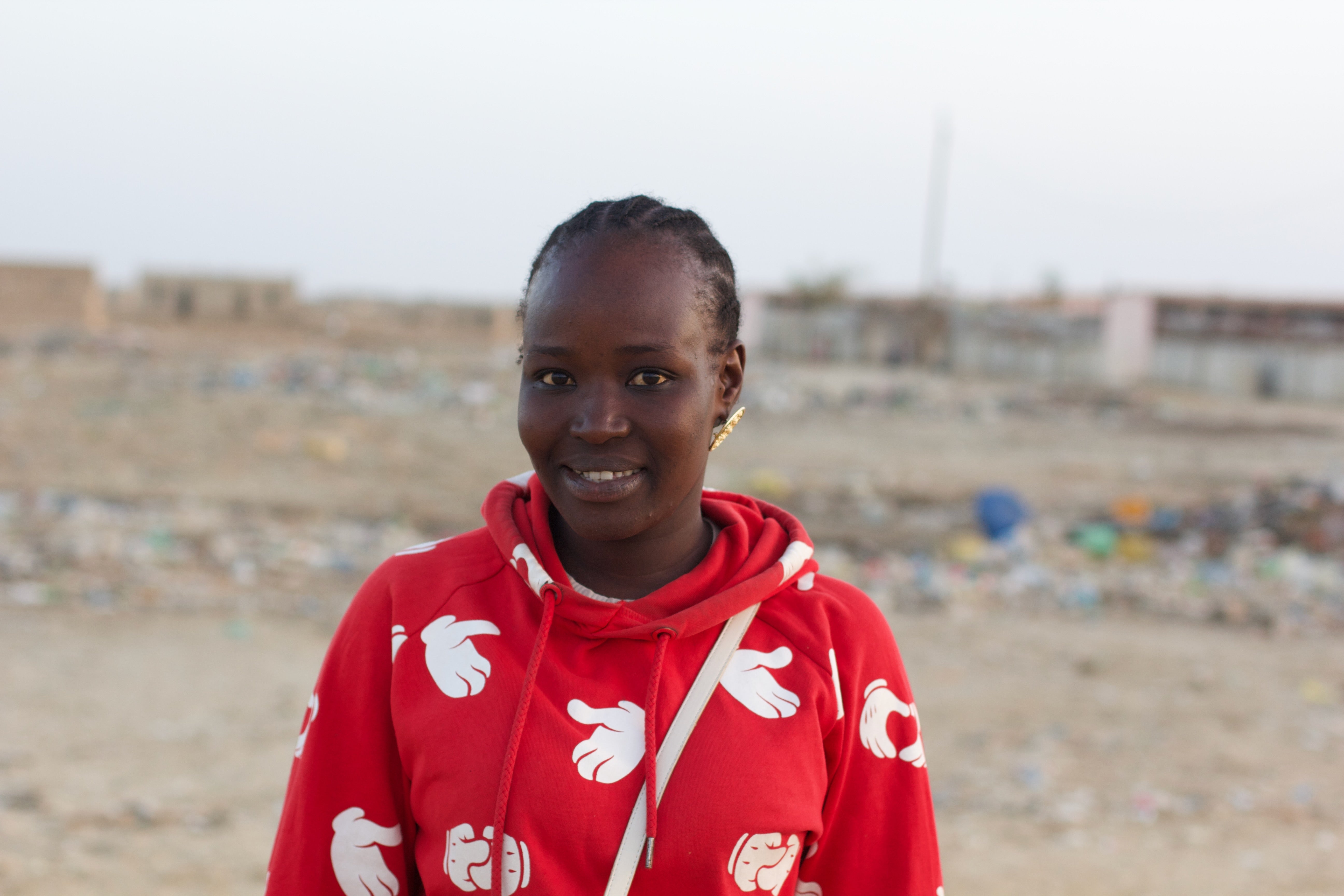 A woman in a red shirt standing in front of a waste dump