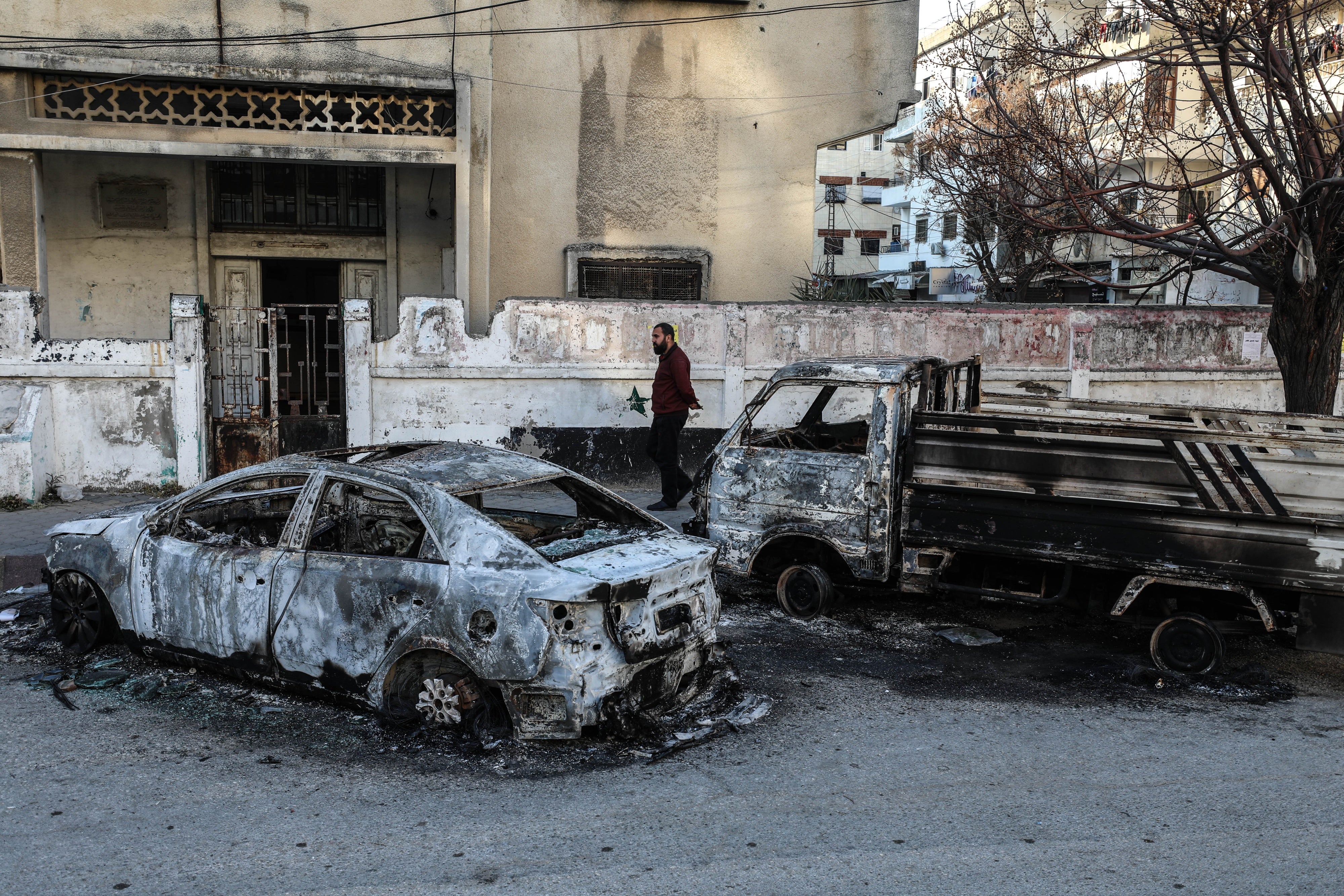 A man walks by burnt cars in a residential area
