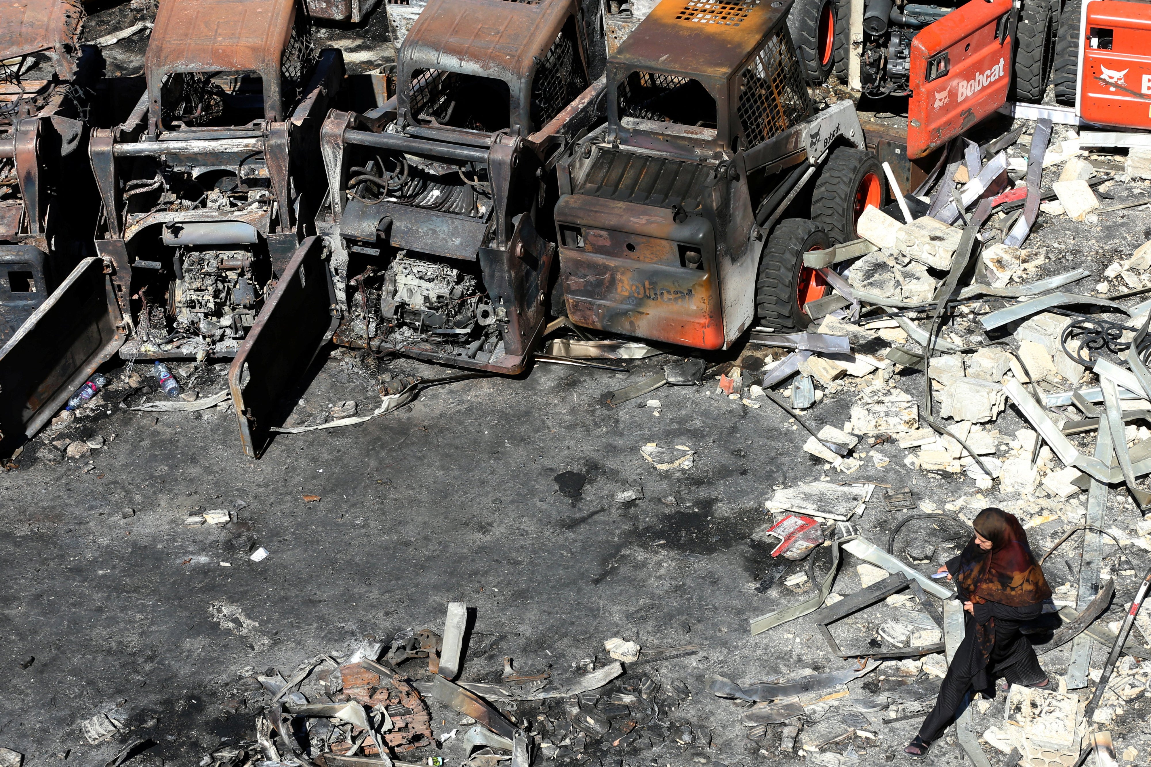 A woman walks in front of charred agricultural equipment, at the site of an Israeli strike in the southern Lebanese village of Msayleh, on October 11, 2025. 