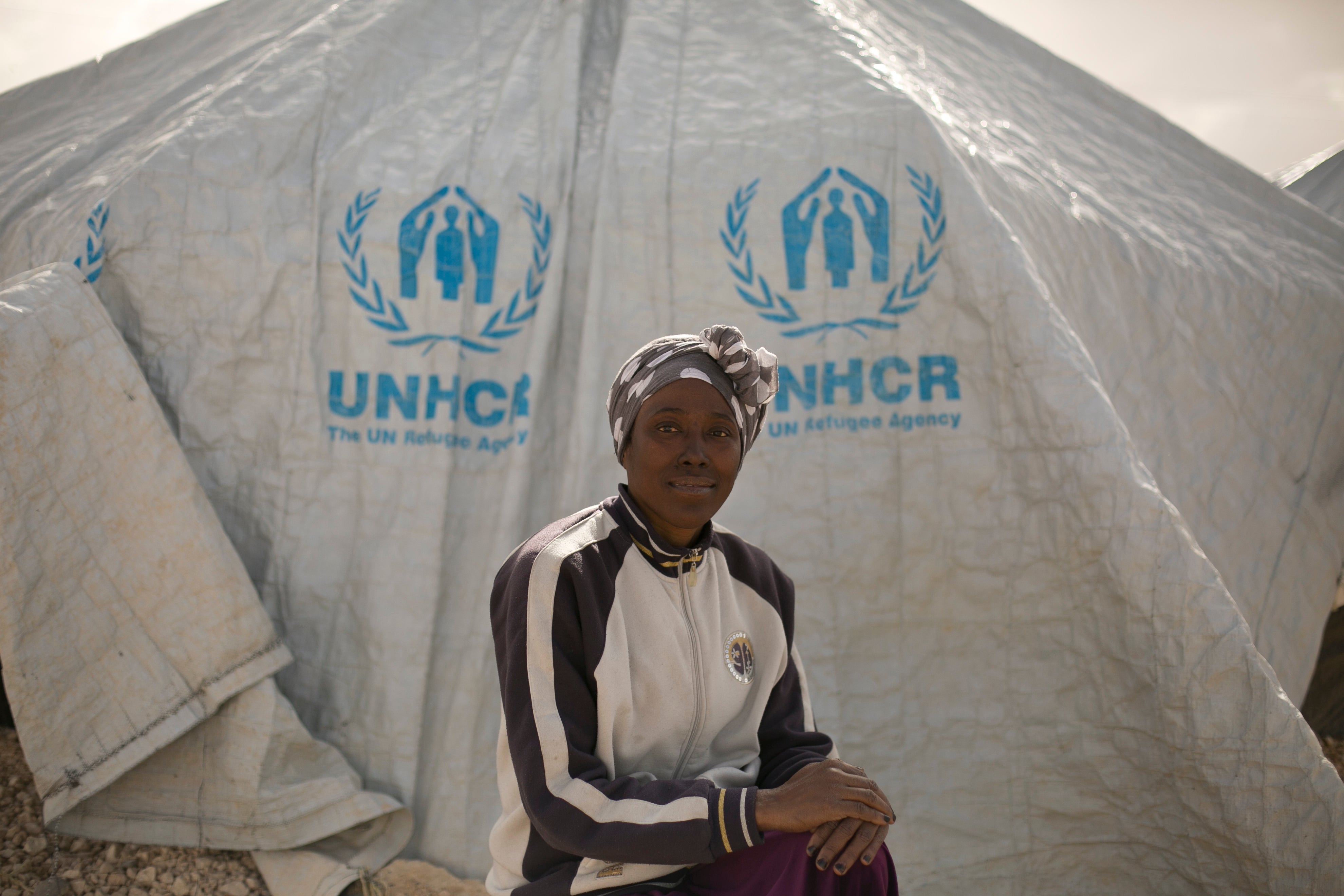 A woman poses for a portrait in front of a UNHCR tent