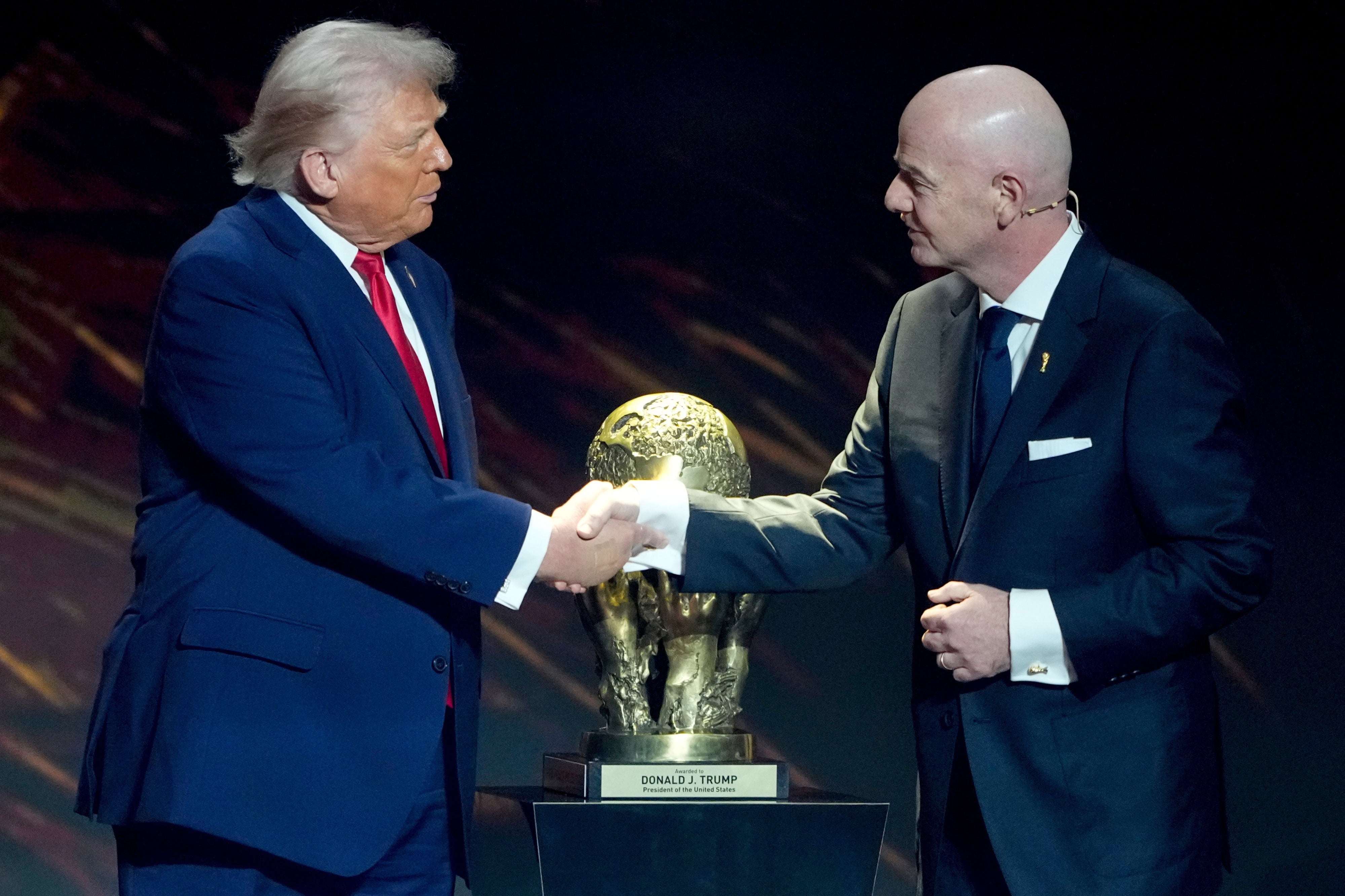 Gianni Infantino shakes Donald Trump's hand in front of the peace prize cup
