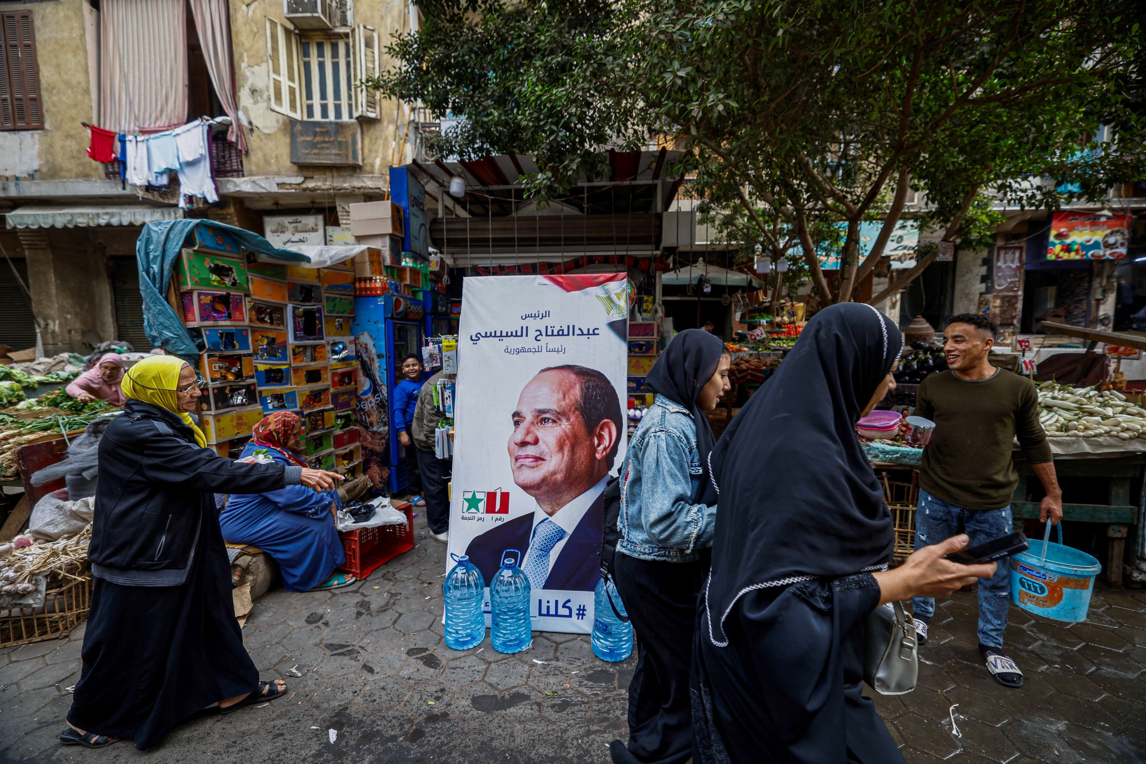 People walk past a campaign poster of Egypt's President Abdel Fattah al-Sisi in a market in Cairo ahead of the presidential election, December 7, 2023.