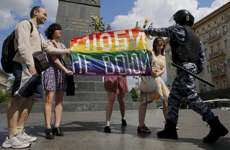 Participants in a LGBT community rally in central Moscow, Russia hold a rainbow flag that reads, "Love. Don't make war", as a policeman stops them.