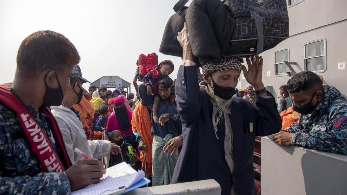 An elderly man carries luggage over his head as he walks he off a ship