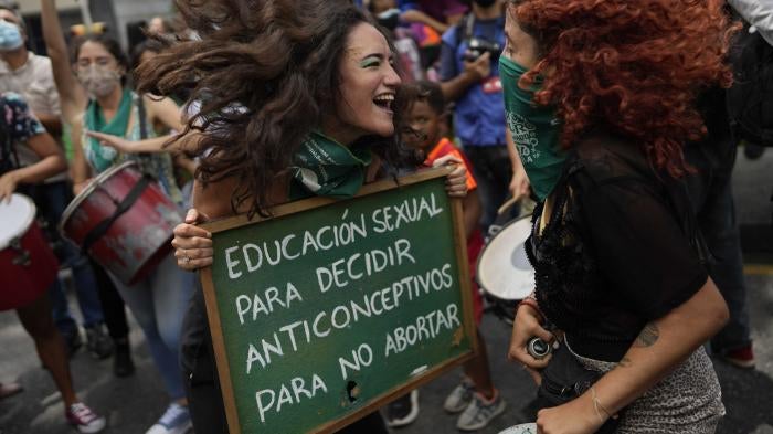 Two women jump and smile while holding a protest sign