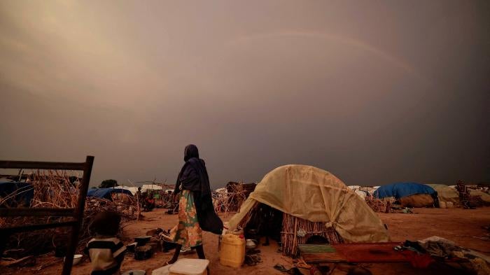 A woman stands by a tent in a refugee camp