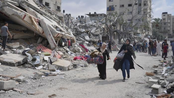 Palestinian women walk by buildings destroyed in Israeli airstrikes in Nuseirat camp in the central Gaza Strip, October 16, 2023.