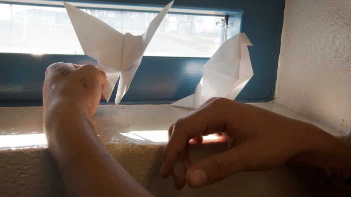 A youth holds two pieces of paper origami in a cell