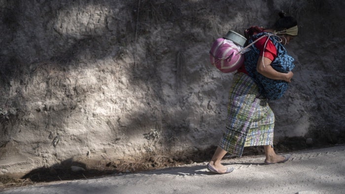 A woman transports water on her back while carrying her youngest son in her arms