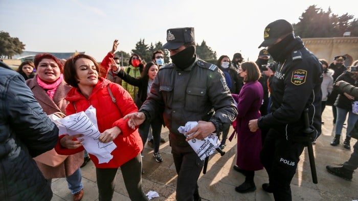 A woman holding a protest sign is surrounded by police