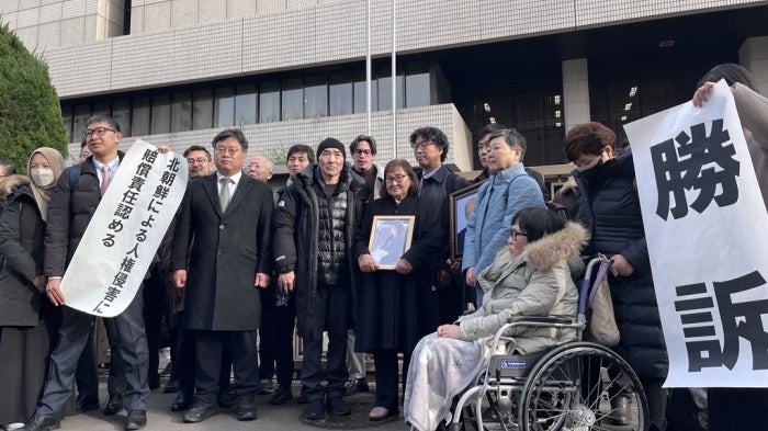 Plaintiffs holding flags declaring the verdict in front of the Tokyo district court main gate, January 26, 2026. 