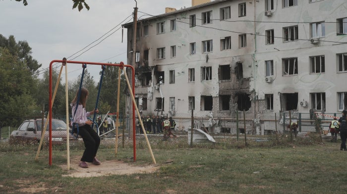 A girl on a swing looks at an apartment building in the Industrialnyi district of Kharkiv, Ukraine, damaged by a Russian drone attack that killed 7 people (including children) and injured 23, on August 18, 2025.