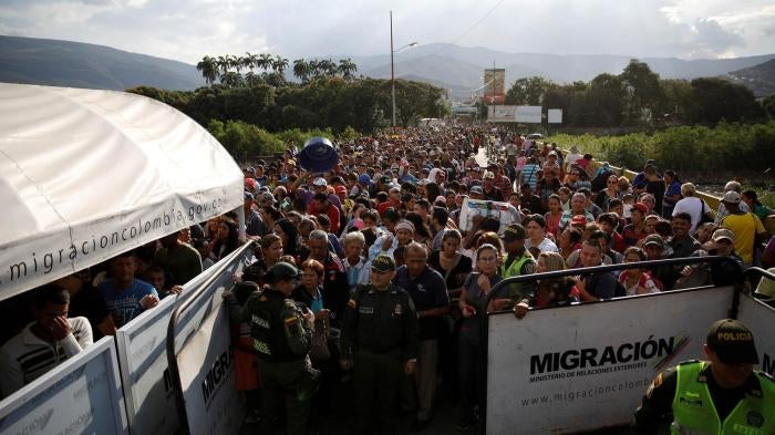 Colombian police officers stand in front of people queueing to try to cross into Colombia from Venezuela through the Simon Bolivar international bridge in Cucuta, Colombia. January 24, 2018.