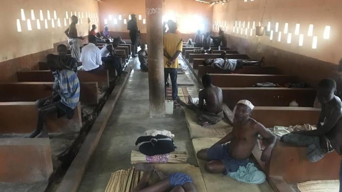 Men sitting on beds and on the floor in a crowded room