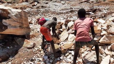 Two boys pick up large rocks at a quarry 