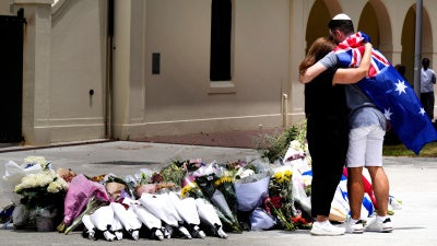 Two people stand hugging in front of flowers.