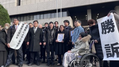 Plaintiffs holding flags declaring the verdict in front of the Tokyo district court main gate, January 26, 2026. 