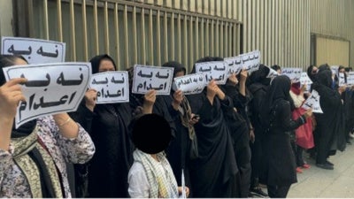 أفراد عائلات أشخاص محكوم عليهم بالإعدام يتجمعون خارج مبنى السلطة القضائية في طهران، إيران، 24 مايو/أيار 2023، حاملين لافتات كتب عليها "لا للإعدام". 