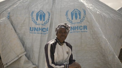 A woman poses for a portrait in front of a UNHCR tent