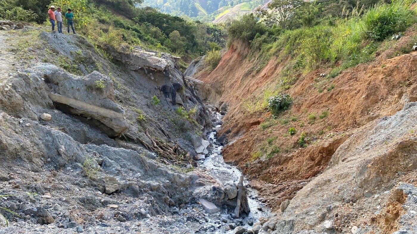  Men peer out over the remains of a portion of the road that had connected the town of Timushan to La Unión, Zacapa state, Guatemala. The road was destroyed during Eta and Iota in November 2020, and has not yet been rebuilt, March 2022.
 © 2022 Max Schoening for Human Rights Watch
