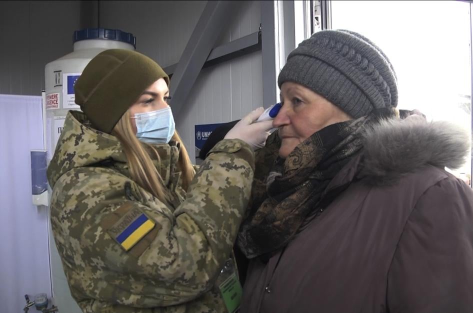 A soldier in a face mask checks the temperature of an older woman at a checkpoint in Mayorsk, Donetsk region, Ukraine, Monday, March 16, 2020.