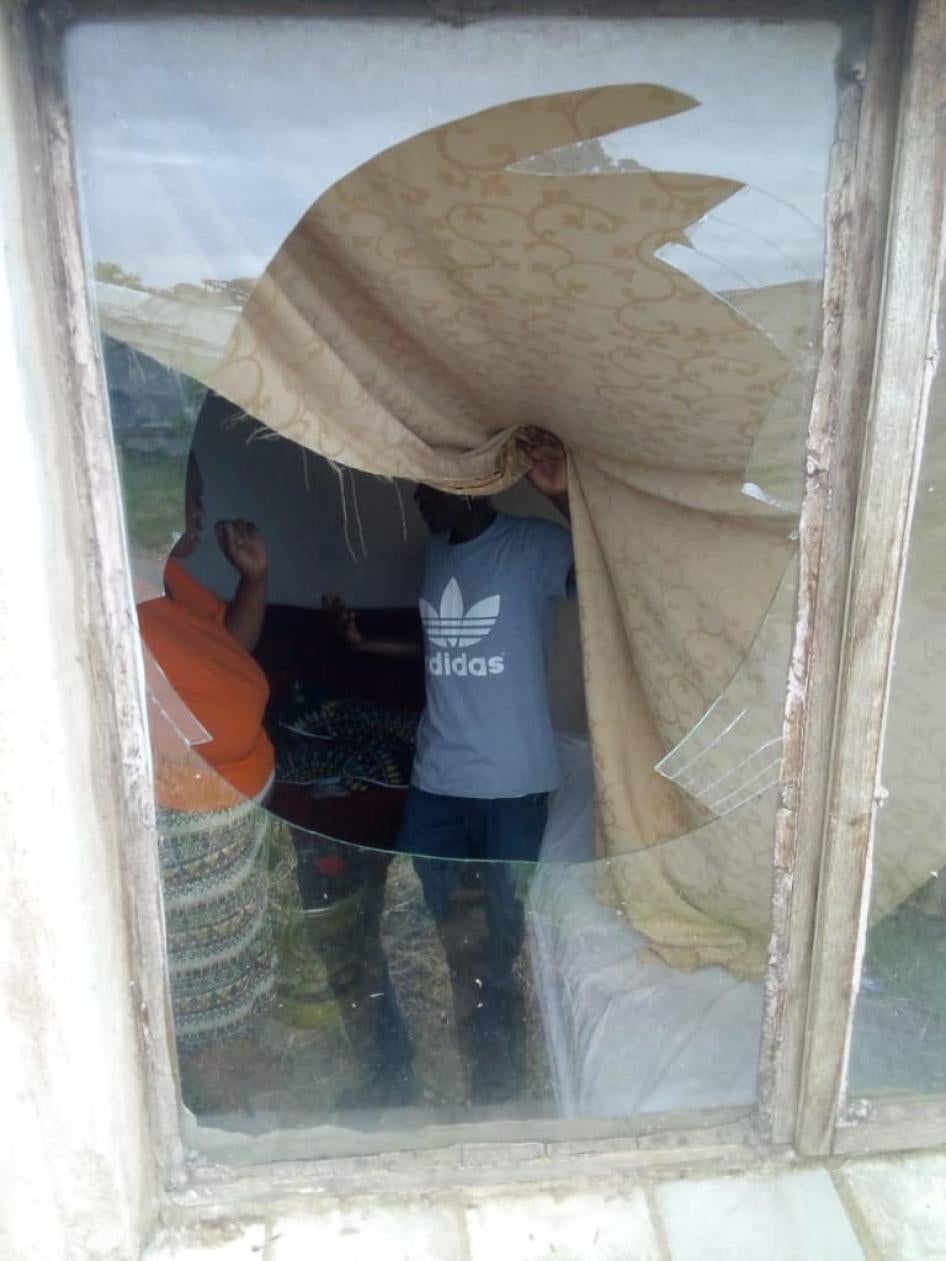 A boy pulls back a curtain to reveal a broken window