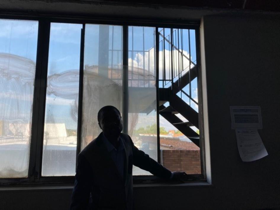 A man poses in his apartment, obscured by shadows