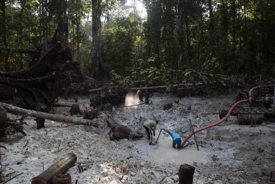 Two people kneel in a mine in a jungle