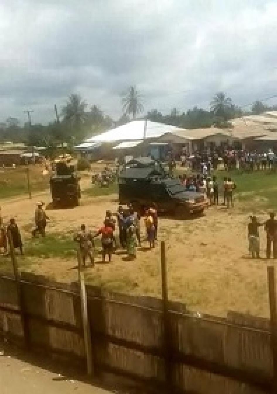 crowd gathered outside school. army vehicle parked. 