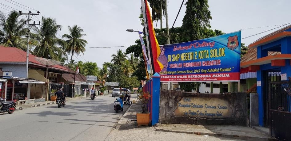 A billboard in front of a school, next to a paved road