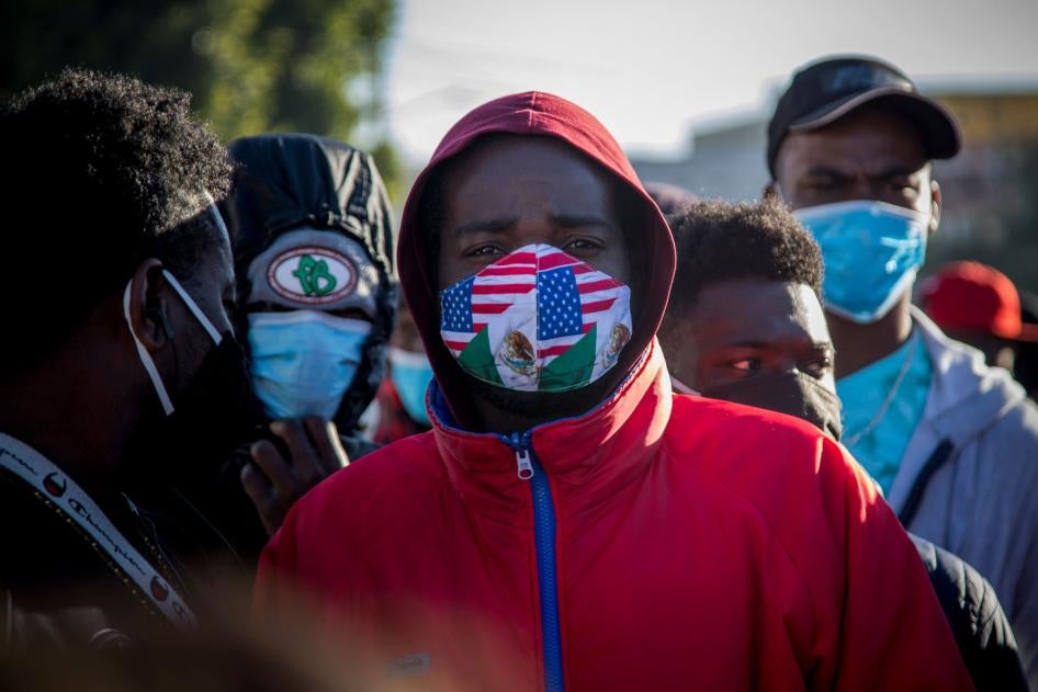 A migrant from Haiti wearing a mask in the colors of the Mexican and US flags stands at a border crossing with others, waiting to asylum in the US, February 19, 2021. 