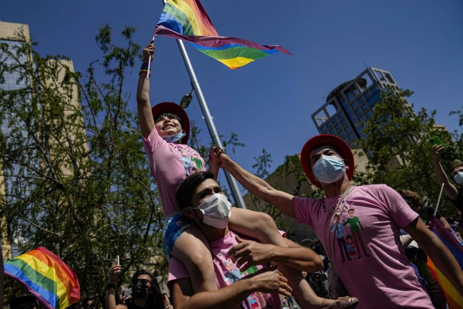 A girl waves a rainbow flag while sitting atop her fathers shoulders