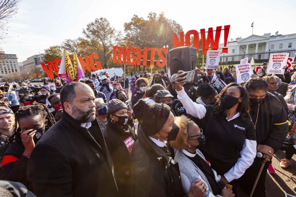 A crowd standing in front of a sign that reads "Voting Rights Now!"