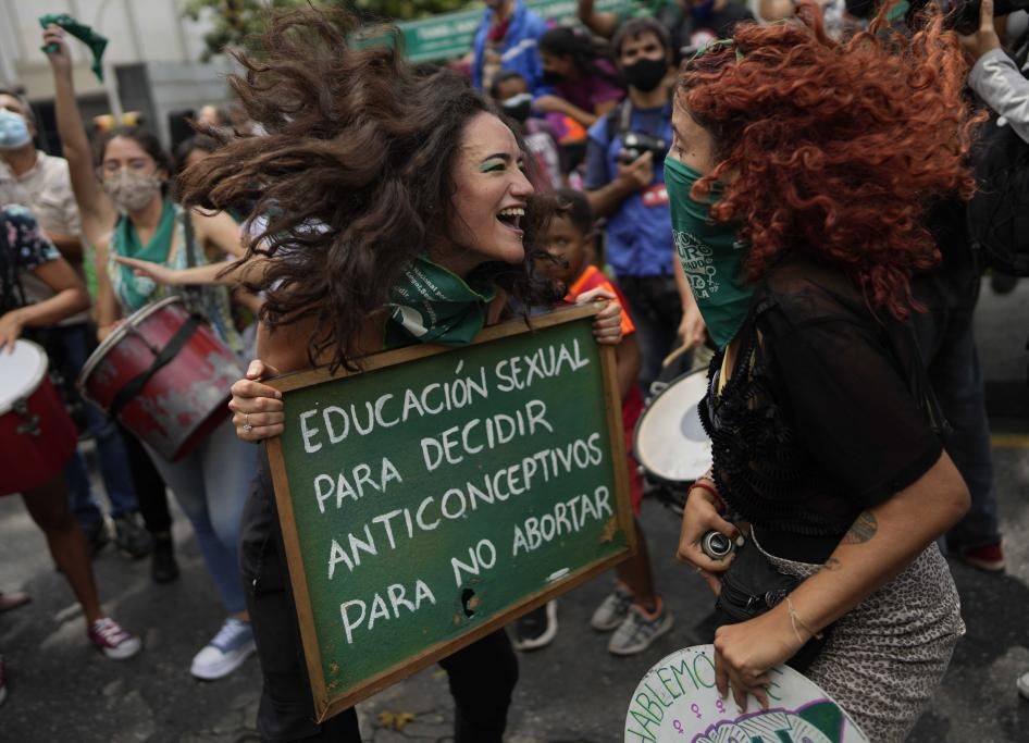 Two women jump and smile while holding a protest sign