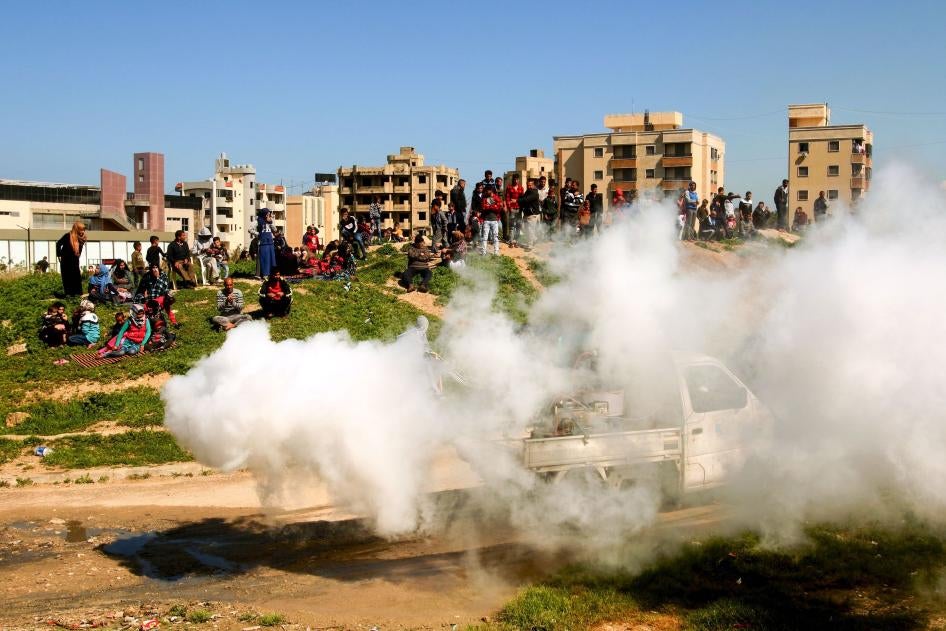 Des réfugiés syriens regardent des travailleurs des services d’assainissement libanais pulvériser du désinfectant près d'un bâtiment en construction qu'ils utilisaient comme abri dans la ville de Sidon, au sud du Liban, le 22 mars 2020, dans le cadre de mesures anti-Covid.