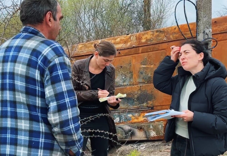 Two women take notes and interview a man outside