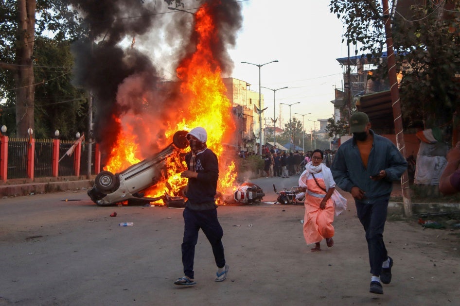 People run past burning vehicles of India's Bharatiya Janata Party (BJP) during a protest to condemn the alleged killing of women and children in Imphal, capital of India's northeastern state of Manipur, November 16, 2024.